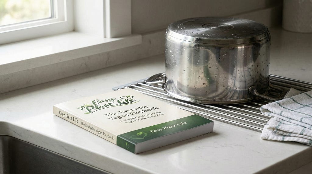 A paperback copy of Easy Plant Life: The Everyday Vegan Playbook on a kitchen counter beside a drying pot